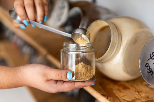 Hands serving bulk ground ginger in a zero waste store into a reusable glass container