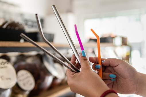 Woman holding, comparing reusable drinking straws in zero waste store