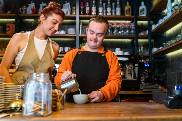 Young man with Down Syndrome working at cafe, preparing coffee Young man with Down Syndrome working at cafe, preparing coffee developmental disability diversity stock pictures, royalty-free photos & images