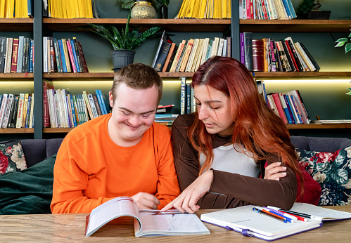 Young man with Down syndrome and his tutor studying indoors