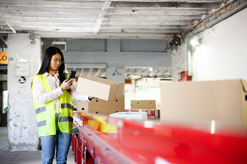 Portrait of an Asian female warehouse worker checking the boxes on the conveyor belt