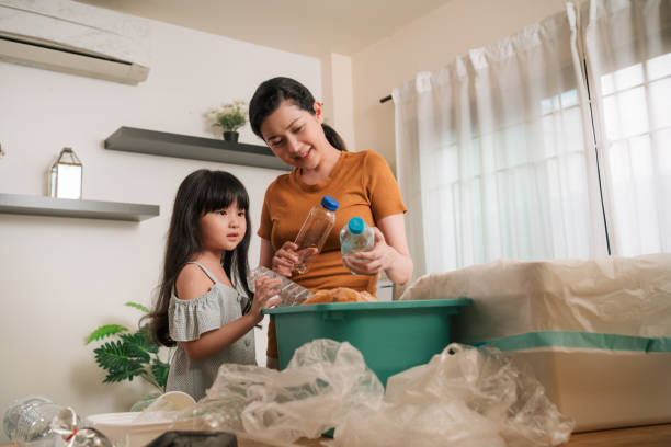 mother teaching daughter sorting out waste for recycling recycle bank help climate change at home - sustainable resources environment education cleaning imagens e fotografias de stock