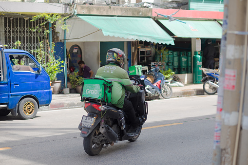 Grab Express delivery person is driving on motorcycle. In his bag is delivery box on motorcycle. He turned from one street into another. Scene is in Chokchai 4 in Bangkok Ladprao