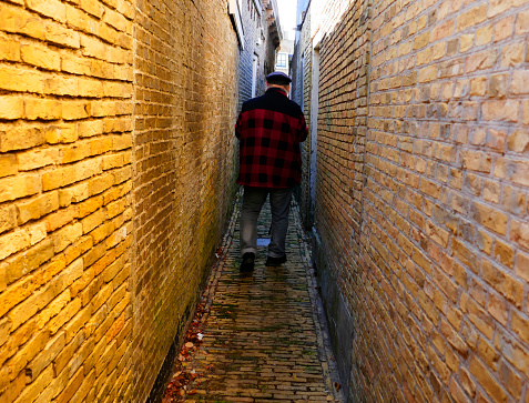 Man with broad shoulders walking down an an extreme narrow alley in Harlingen, the Netherlands