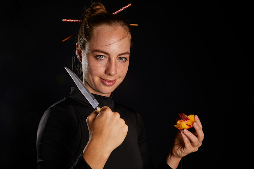 young girl in black suit holding fruit and knife at hand posing towards camera with happy and confident face