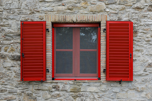 Window with open red shutter, brick stone house wall with rough and uneven surface, no person
