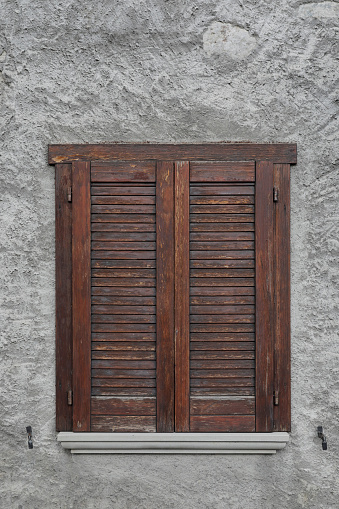 An old wooden window frame with broken windows and flaking paint looking into a dark room