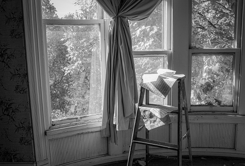 Sheet music cascades off a ladder in front of a curtained window in an abandoned old house.