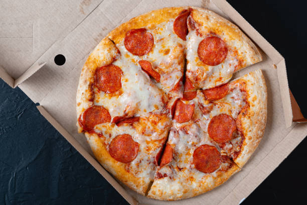 istock Pizza in a cardboard box on a black chalkboard background. View from above. Pizza delivery. Pizza menu 1433659472