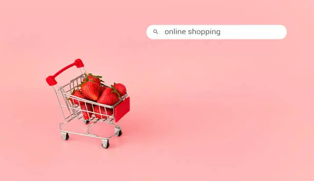 Fresh red strawberry in shopping card on pink background with search box. Online shopping and Valentines Day minimalistic concept. Black Fridays sales banner. Healthy, organic, vegan food.