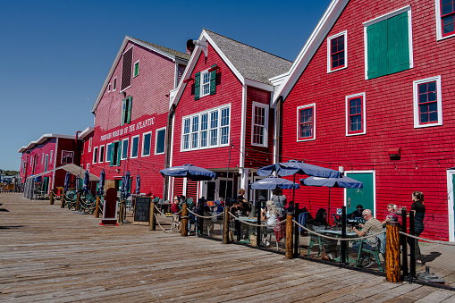 Lunenburg, Nova Scotia, Canada -- Sept 17,2022. A photo taken with a wide angle lens along the Lunenburg boardwalk that includes an outdoor dining area and the exterior of a museum.