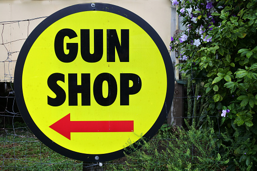 A round yellow and black Gun Shop sign with red arrow pointing to the left direction.