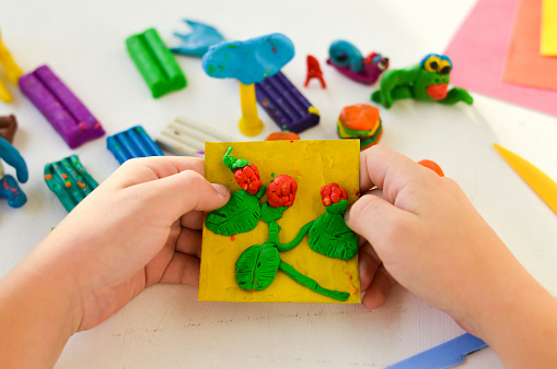 A close-up of hands with plasticine, children's crafts and an application on the theme of harvest.