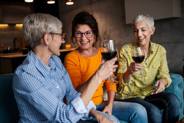 Happy senior woman toasting with her husband at home while drinking red wine.