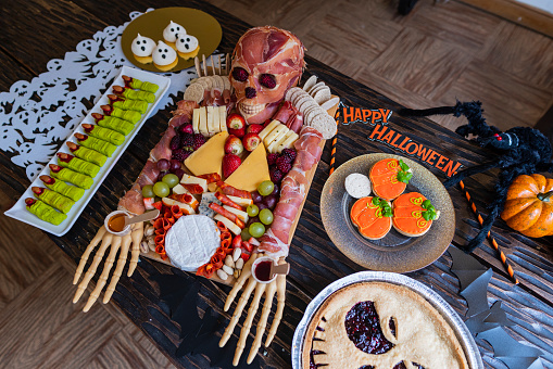 Female chef prepares a delicious cheese board for halloween using pumpkin skulls and delicious ingredients
