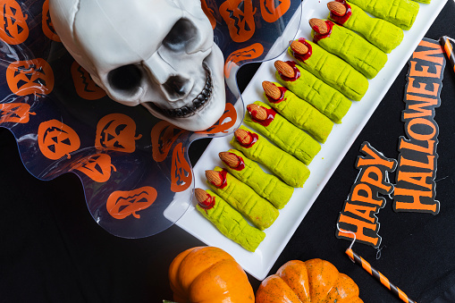 Delicious shortbread cookies in the shape of green fingers for Halloween with pumpkins and skull background