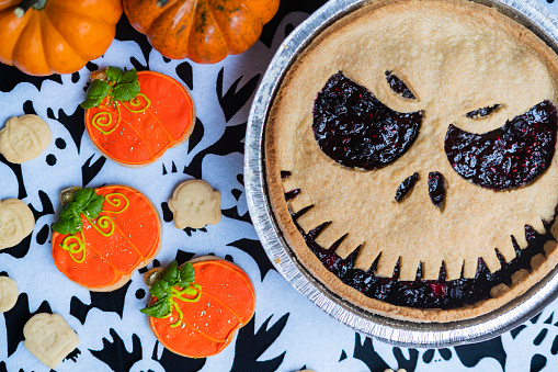 Delicious blackberry cake with a scary face for Halloween and cookies in the shape of a pumpkin
