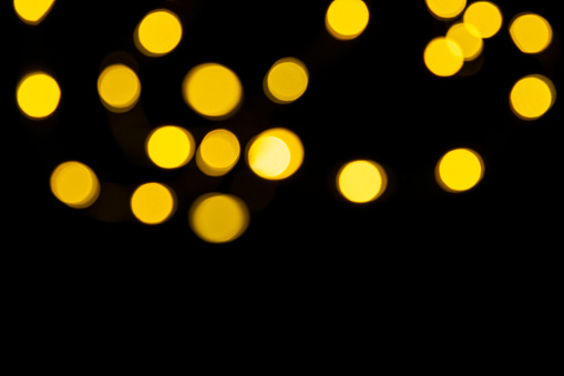 Golden blurred lighs bokeh on black background as a festive backdrop, night defocused light spots