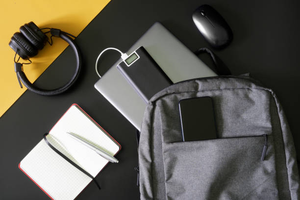 istock Compact urban backpack with laptop, external battery - power bank, mobile phone, headphones,  mouse, notepad and pen on black and yellow background. Study, travel and trip with gadgets. 1433678311