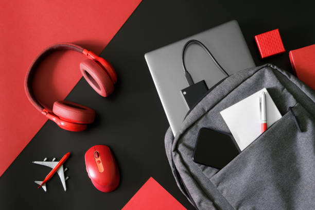 istock Gray urban backpack with a laptop, ssd drive, phone, notepad and pen on black and red next to mouse, headphones and toy plane. Gadgets and luggage of students, IT people and journalists. 1433678364