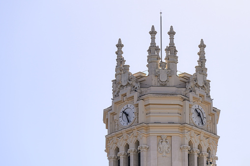 Madrid, Spain - September 25, 2022: Clock tower of a building against a blue sky. There are two clock faces on the tower, and no people are on the scene.