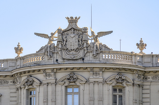 Madrid, Spain - July 18, 2022: Low angle view of the upper part of Palacio de Linares at Cibeles square. The top of the building has a decorative sculpture depicting two angles holding a banner.