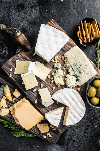 Delicious Cheese board.  Assortment of cheese, camembert, brie, Gorgonzola, parmesan, olives, nuts and herbs. Black background. Top view.