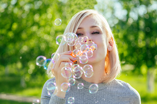 attractive blonde girl blowing soap bubbles in the park on a background of green grass . bubble and holiday atmosphere.