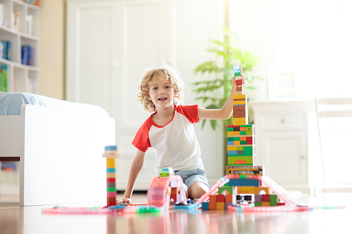 Kids play with colorful blocks. Little boy building tower at home or day care. Educational toy for young child. Construction creative game for baby or toddler kid. Mess in kindergarten playroom.