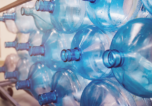 Empty bottles are stacked in a row. Cleaning of plastics in the production of pure water. Background from blue bottles with backlight. Environmental problem due to plastic in everyday life
