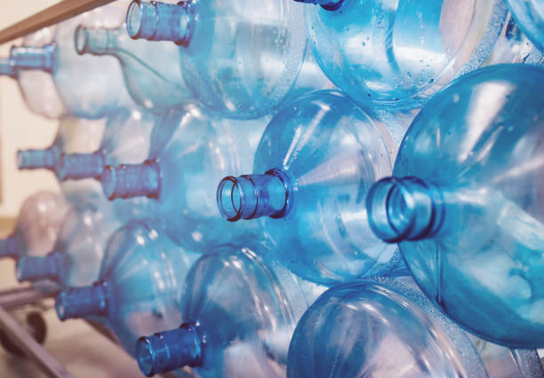Empty bottles are stacked in a row. Cleaning of plastics in the production of pure water Empty bottles are stacked in a row. Cleaning of plastics in the production of pure water. Background from blue bottles with backlight. Environmental problem due to plastic in everyday life water cooler stock pictures, royalty-free photos & images