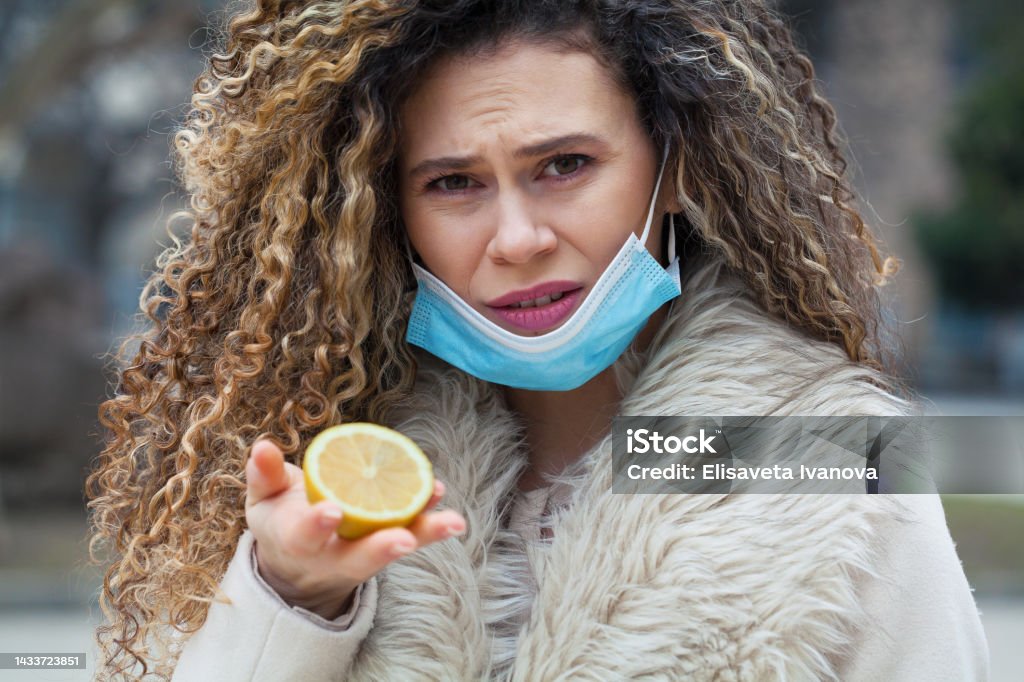 Taste and smell loss COVID-19 symptom Young woman with a protective face mask smelling a sliced lemon 20-29 Years Stock Photo