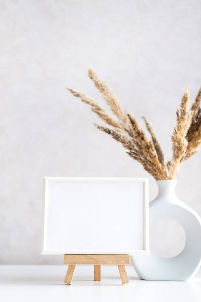 istock Empty picture frame mock up in minimalist interior with dried plant in vase on white table. 1433741934