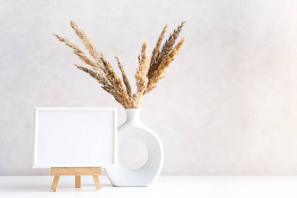 istock Empty picture frame mock up in minimalist interior with dried plant in vase on white table. 1433741935
