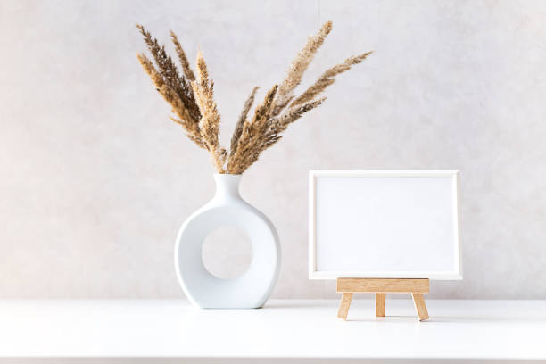 istock Empty picture frame mock up in minimalist interior with dried plant in vase on white table. 1433741937