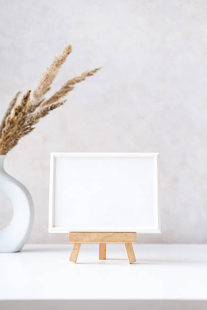 istock Empty picture frame mock up in minimalist interior with dried plant in vase on white table. 1433741938