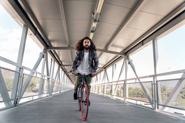 Handsome hipster man with long hair looking at front and riding his bike in the city.