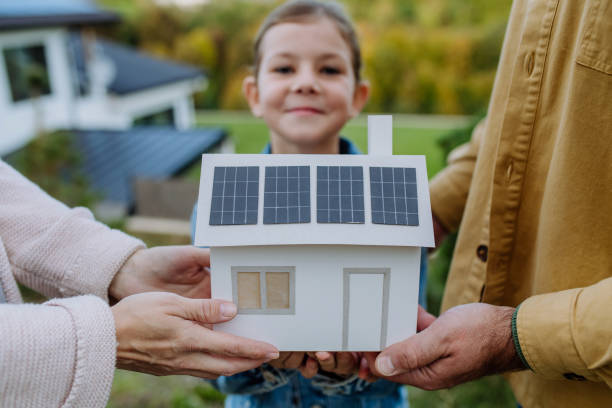 Close up of young family holding paper model of house with solar panels.Alternative energy, saving resources and sustainable lifestyle concept. stock photo