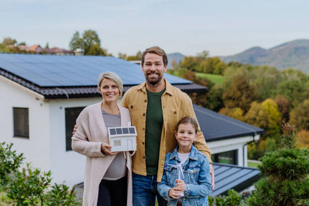 Happy family holding paper model of house with solar panels.Alternative energy, saving resources and sustainable lifestyle concept. stock photo