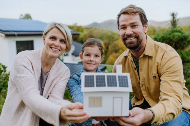 Happy family holding paper model of house with solar panels.Alternative energy, saving resources and sustainable lifestyle concept. stock photo