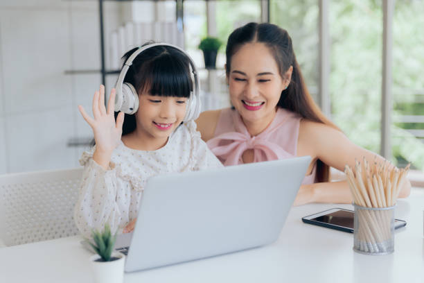 istock Attractive asian mom teaching little cute daughter in headphone learning online class with computer laptop at home, Online e-learning education concept 1433754235