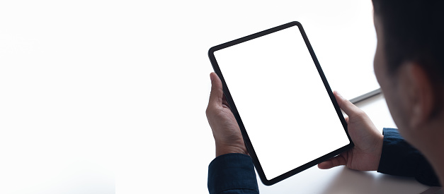 Mockup image of man's hand holding black white screen digital tablet on white black ground, over shoulder view