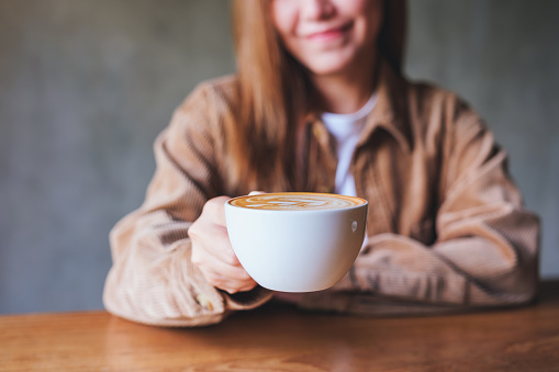 Closeup image of a young woman holding and serving a cup of hot coffee