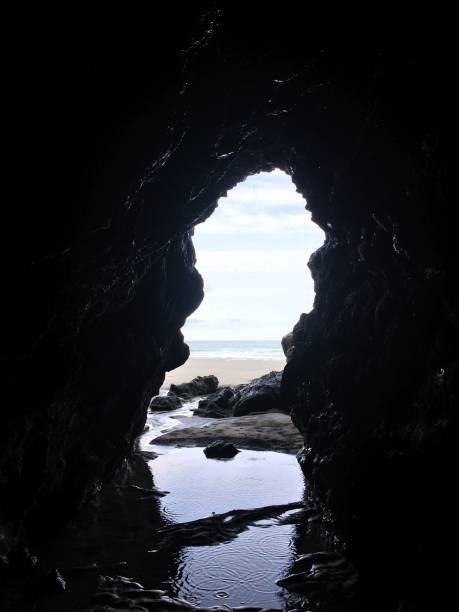 istock Inside a black natural sea cave with a brightly lit opening onto a golden sand beach 1433757798