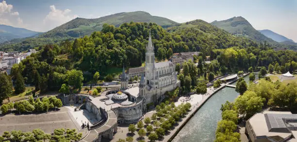 Famous Sanctuary of Our lady of Lourdes - Rosary Basilica Drone XXL Panorama - World famous Pilgrim destination. Cathedral of Lourdes,  Grotte de Massabille next to river Gave de Pau. Lourdes is a small market town lying in the foothills of the Pyrenees, famous for the Maria apparitions of Our Lady of Lourdes that are reported to have occurred in 1858 to Bernadette Soubirous. Our Lady of Lourdes Basilica in Lourdes, Lourdes,  Hautes-Pyrenees, France, Europe