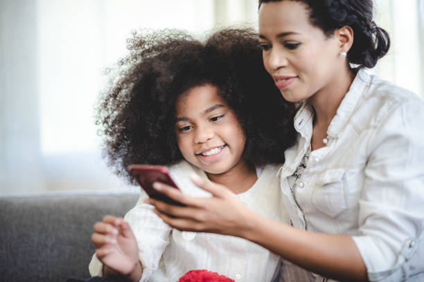 istock Cheerful young mother taking a selfie using smartphone with sister with curly hair while making funny facial and hand gestures sitting on couch at home 1433758985