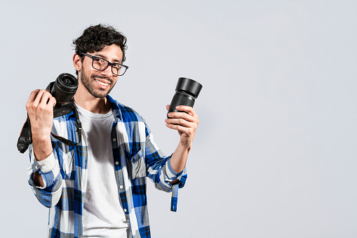 Portrait of smiling photographer man showing a camera and lens on isolated background. Smiling young man holding a camera isolated, Smiling photographer guy showing a camera and lens