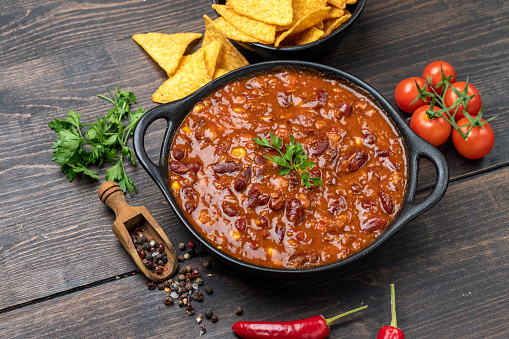 Mexican food chili con carne dish with corn chips nachos on a wooden backdrop.