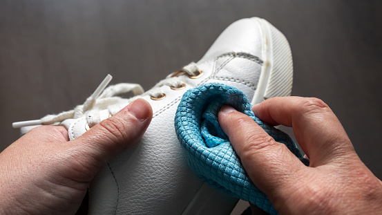 Hands cleaning a white sneaker, with out of focus background