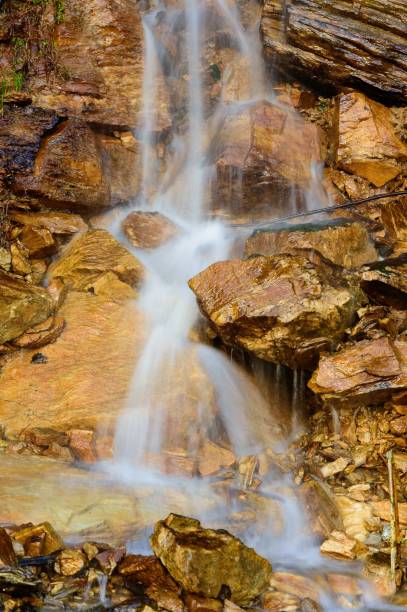 istock Beautiful vertical shot of a waterfall running down a cliff with sharp, wet brown rocks beneath 1433789272